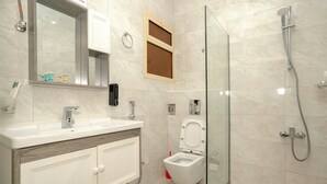 Une salle de bain moderne dotée d’une douche à parois de verre, d’un lavabo blanc avec un plan de toilette en bois et de toilettes avec une structure en bois.