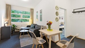Un salon moderne avec un canapé, des fauteuils, une table, une plante en pot et une fenêtre avec des rideaux.