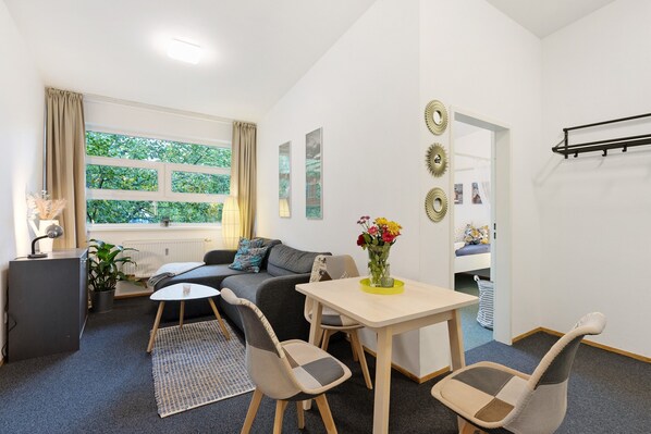 A modern living room with a sofa, chairs, a table, a potted plant, and a window with curtains.