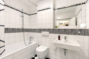 A modern bathroom with a bathtub, toilet, and sink, featuring black and white patterned tiles and a mirror.