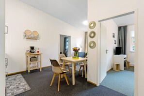 A compact living space with a dining table, chairs, a small kitchen area, and a TV.