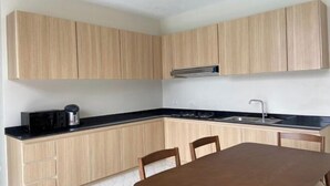 Une cuisine moderne avec des meubles de couleur bois clair, un plan de travail noir, un évier en acier inoxydable et une table à manger avec des chaises.