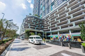 Un edificio moderno de varios pisos con fachada curva, un estacionamiento con una camioneta blanca y una escultura colorida en primer plano.