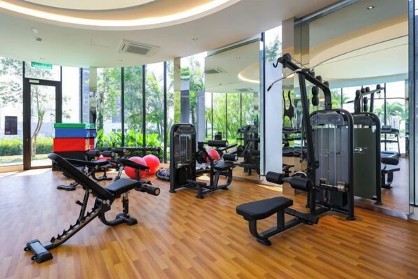 Un gimnasio con diversos equipos de ejercicio, amplias ventanas y piso de madera.