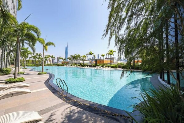 A swimming pool with a curved edge, surrounded by palm trees and lounge chairs, with a city skyline in the background. - Trion KL by Vivid Stay (Kuala Lumpur)