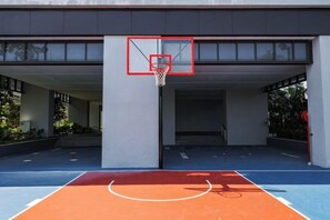 Cancha de baloncesto al aire libre con aro, rodeada por una zona techada con escaleras de acceso.