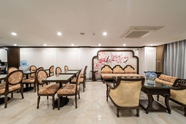 A hotel dining area with multiple tables and chairs, a decorative wall, and a seating area with sofas and a vase.