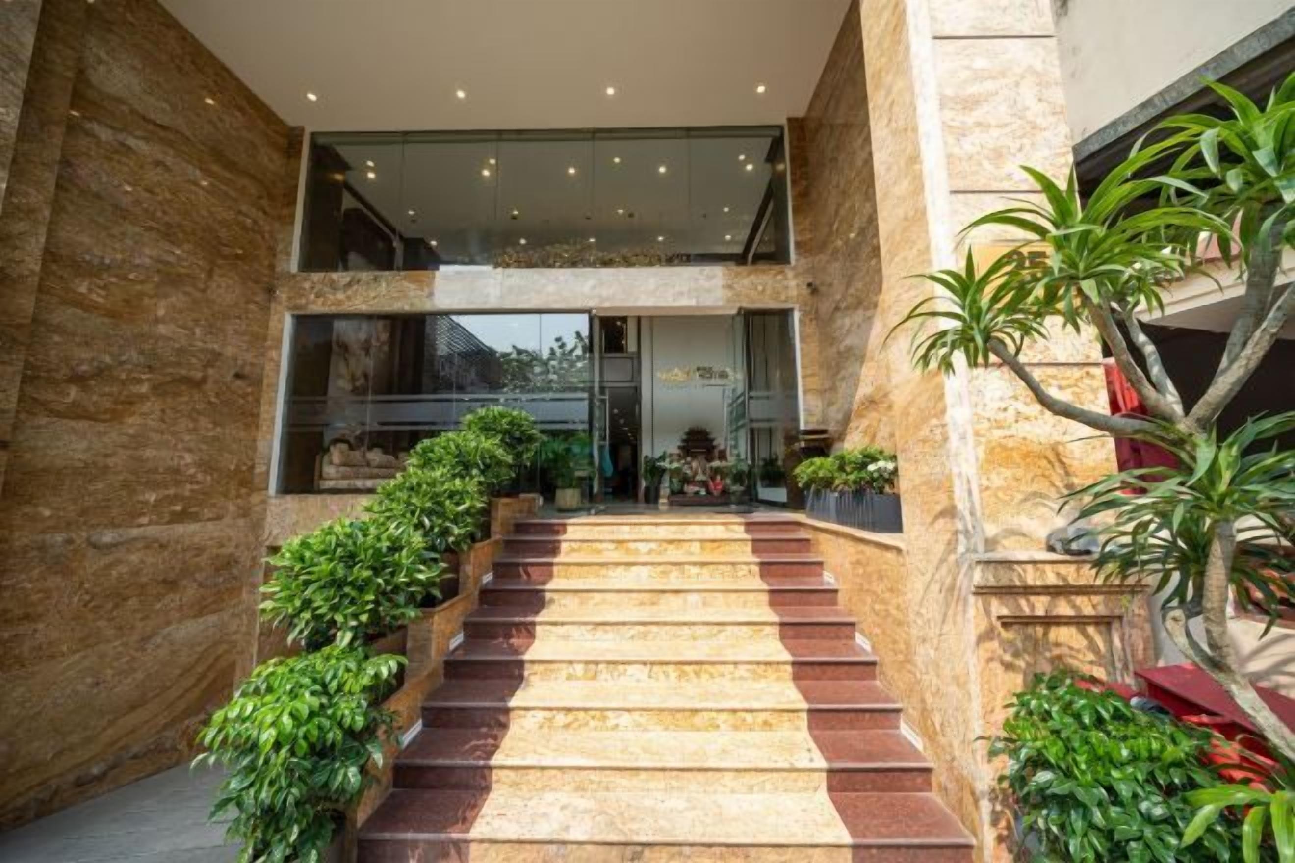 A staircase leading to a modern building entrance with a glass facade, surrounded by greenery.