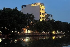 Ein Gebäude mit einem markanten Turm, einem Spiegelbild im Wasser und Bäumen im Vordergrund.