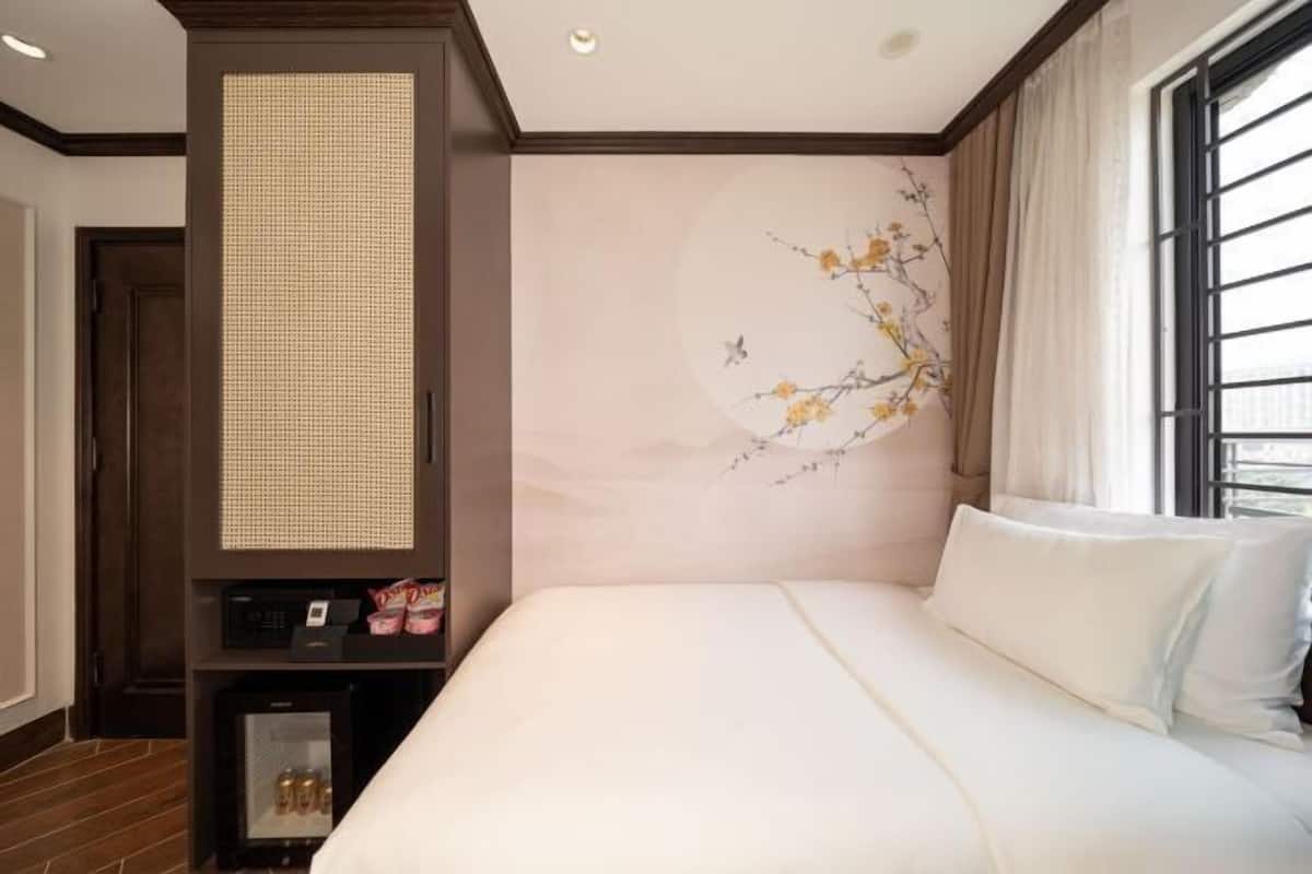 Habitació d'hotel amb un llit, una televisió penjada a la paret, un mini bar i una finestra amb cortines.