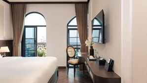 A hotel room with a large bed, a desk with a chair, a mirror, and a view through arched windows. - Legend Smart Hotel (Hanoi)