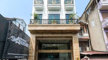 A hotel entrance with a glass facade, a balcony with decorative railings, and a sign above the entrance.
