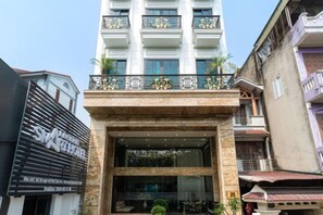 A hotel entrance with a glass facade, a balcony with decorative railings, and a sign above the entrance. - Legend Smart Hotel (Hanoi)