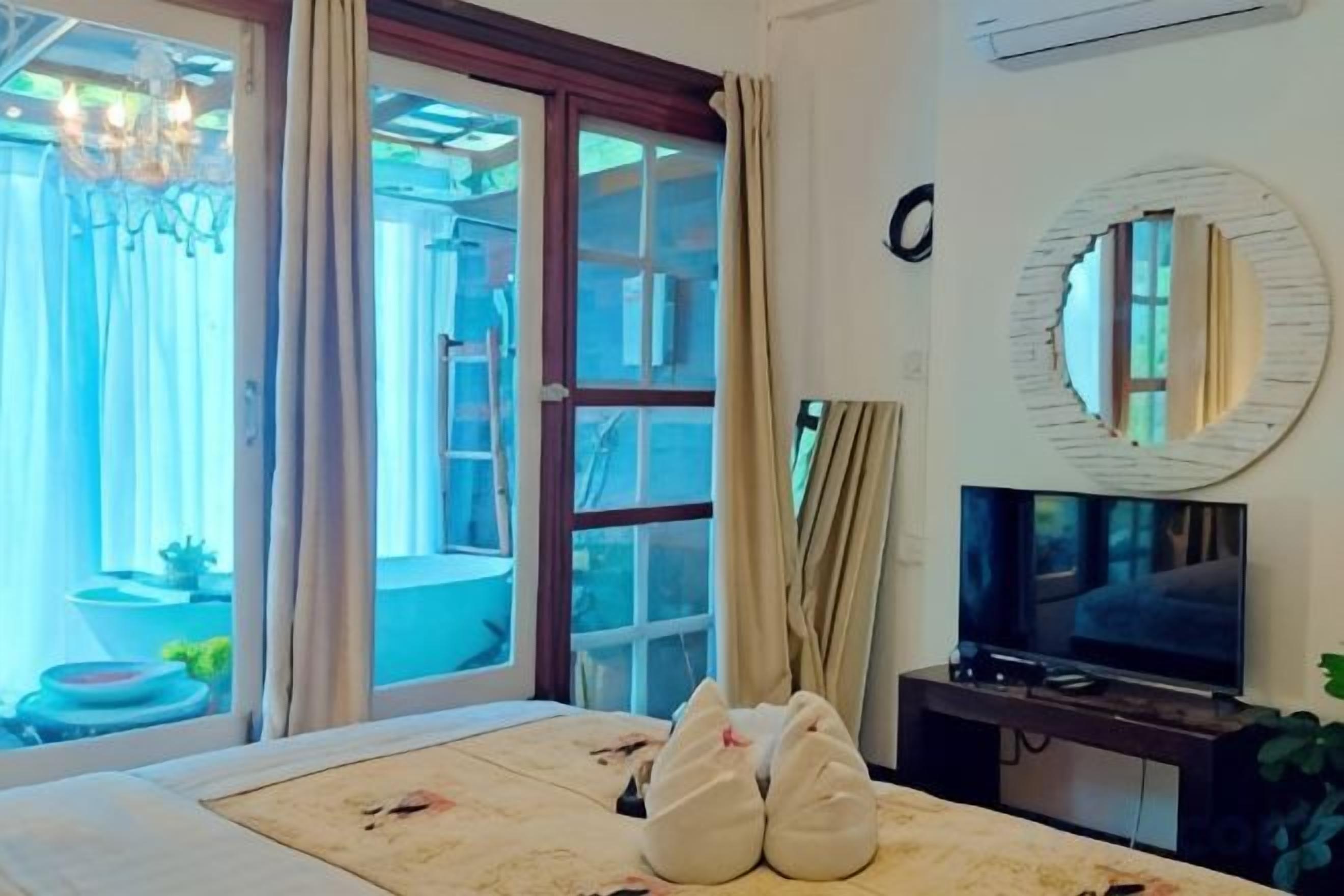 A hotel room with a bed, a television, and a sliding glass door leading to an outdoor area.