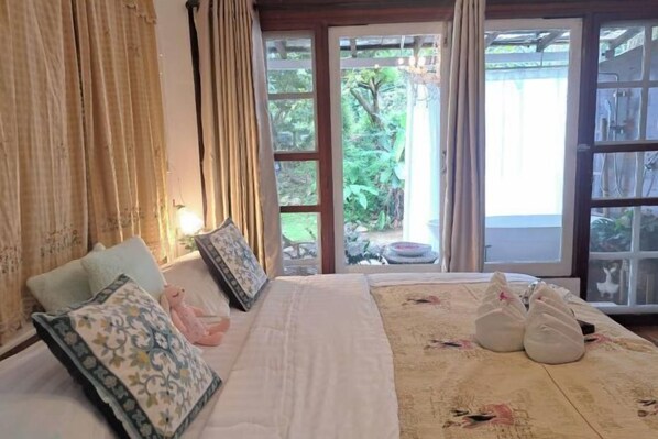 A hotel room with a bed, pillows, and a view of greenery outside.