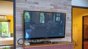 Un téléviseur à écran plat fixé au mur, qui est fait de pierres, et placé au-dessus d’un meuble rose muni de tiroirs.