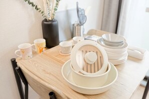 Una mesa de madera con un juego de utensilios de cocina blancos, que incluye un colador y cuencos, y un florero con hojas verdes.