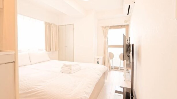Una habitación de hotel con cama, escritorio, silla, ventana con cortinas y una lámpara en el techo.