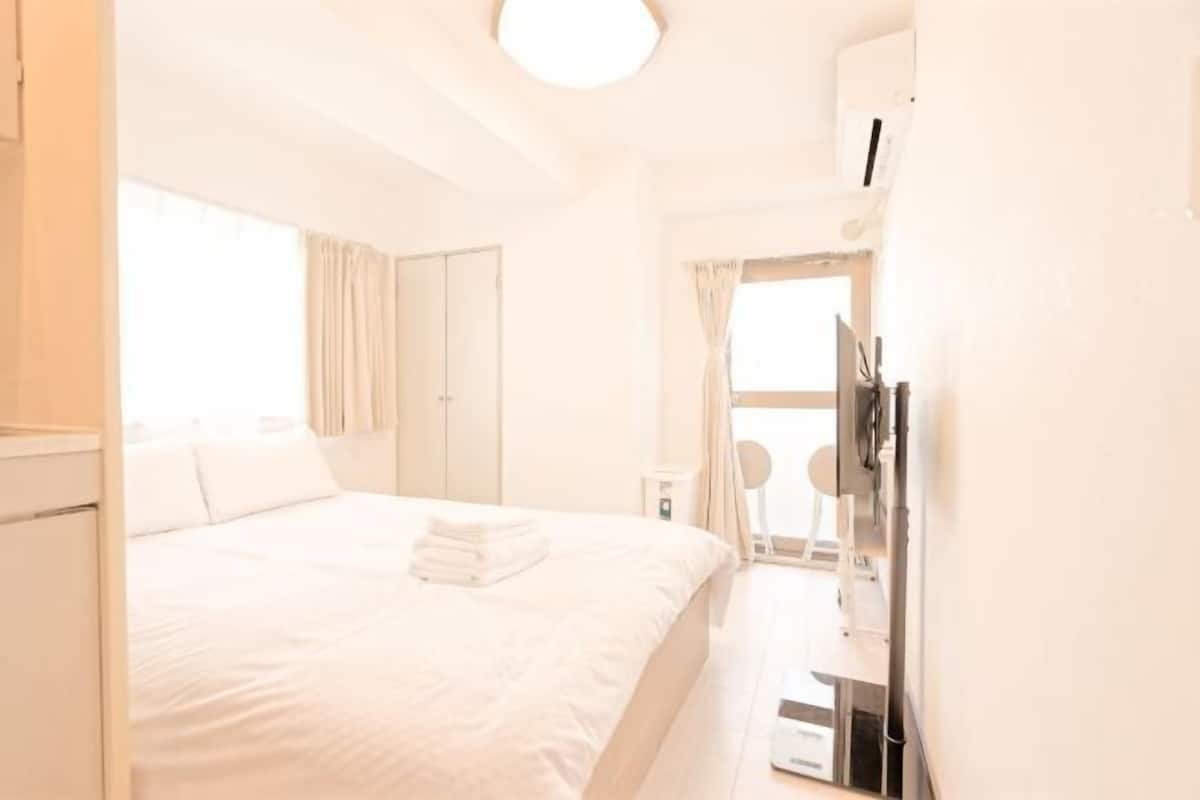 A hotel room with a bed, a desk, a chair, a window with curtains, and a ceiling light.
