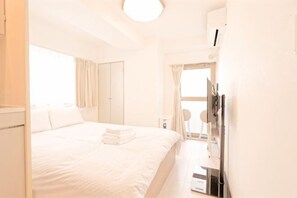 Una habitación de hotel con cama, escritorio, silla, ventana con cortinas y una lámpara en el techo.