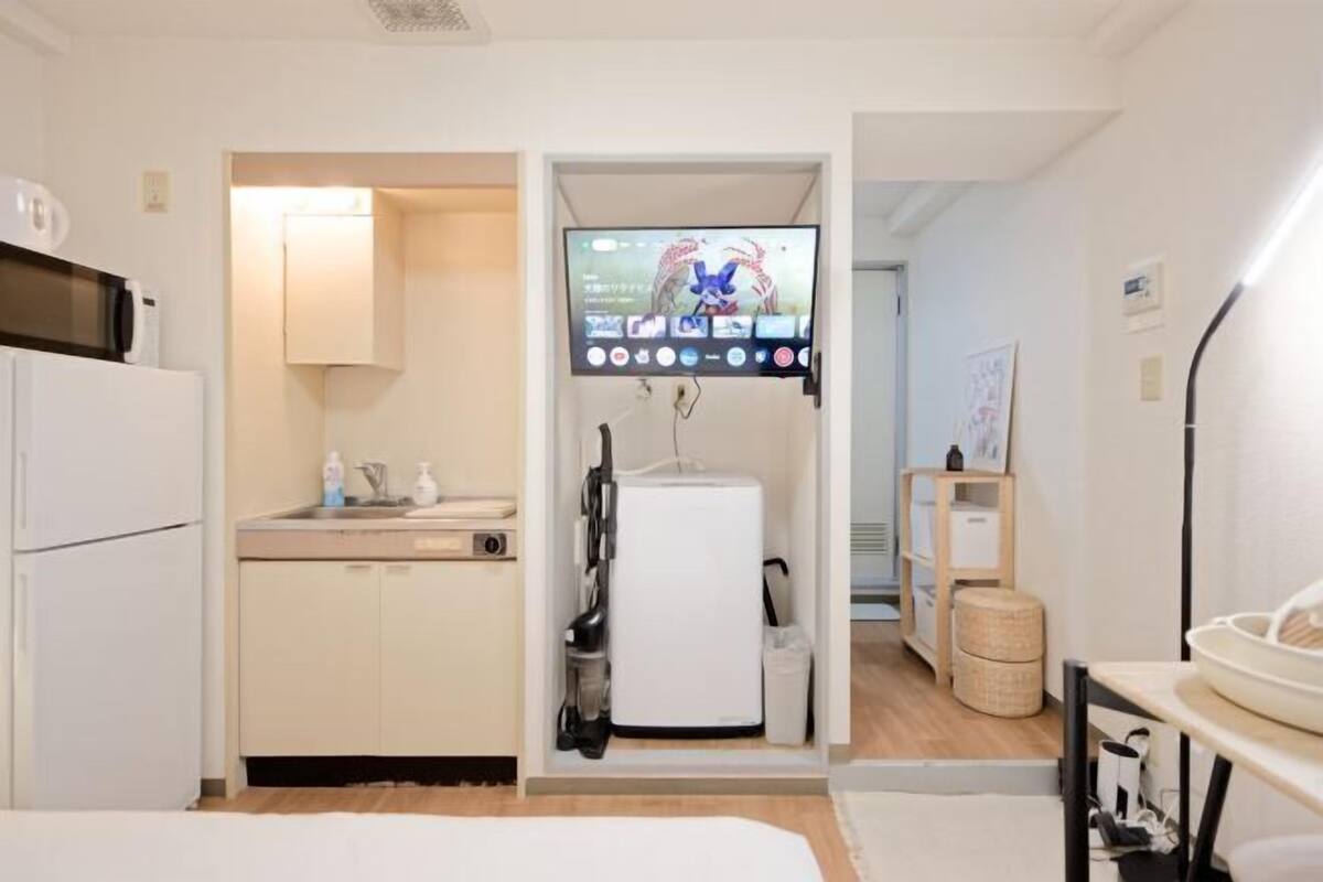 A compact hotel room with a kitchenette, a TV mounted on the wall, and a small seating area.