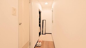 Un pasillo estrecho con piso de madera, una puerta blanca a la izquierda y un espejo a la derecha.