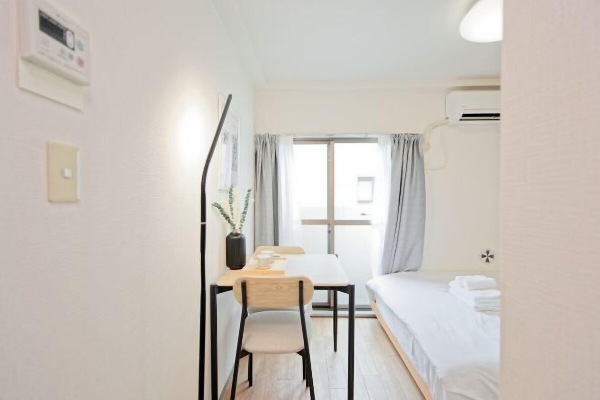Habitación de hotel con cama, escritorio y silla, ventana con cortinas y unidad de aire acondicionado.