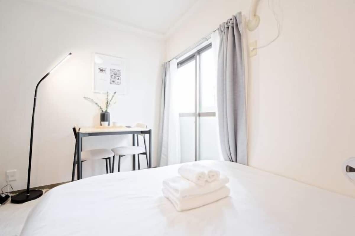 A hotel room with a bed, a desk, a chair, a lamp, and a window with curtains.
