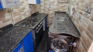 Une cuisine compacte équipée d’une cuisinière à gaz, d’un lave-linge encastré, d’un évier et de meubles de couleur bleue.