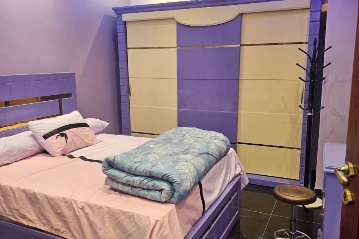 A bedroom with a bed, a wardrobe, and a small stool.