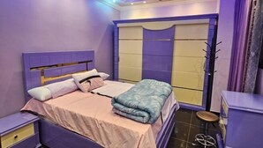 A bedroom with a bed, nightstands, a wardrobe, and a stool. - Susan's Guest House and Tours (Luxor)