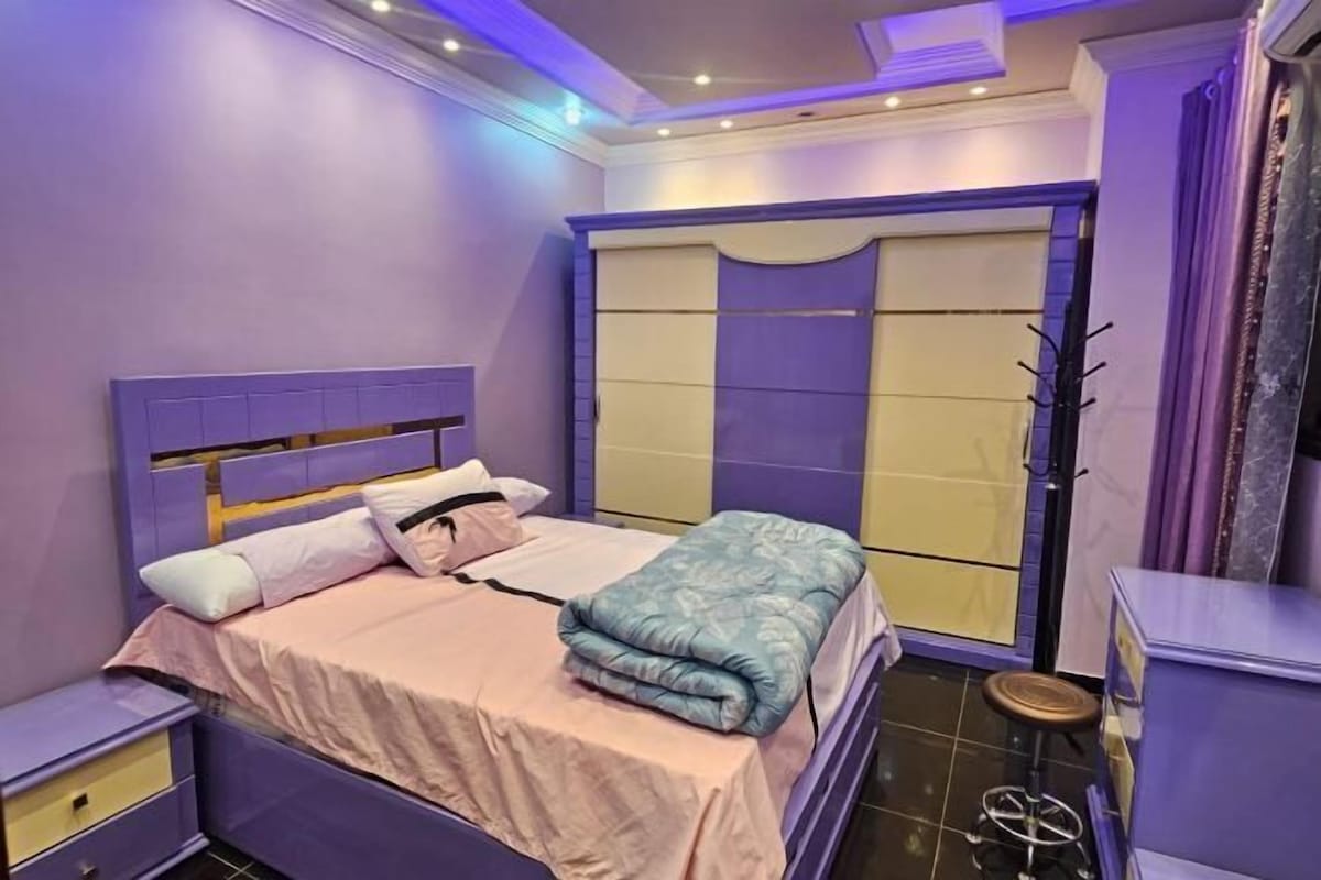 A bedroom with a bed, nightstands, a wardrobe, and a stool.