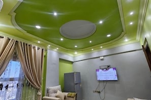 Una habitación con techo verde, una cama, un escritorio y un televisor montado en la pared.