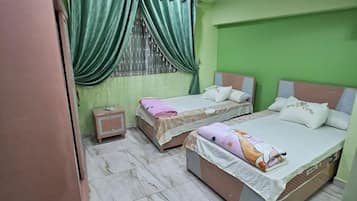 A bedroom with two single beds, a nightstand, and a window with green curtains.