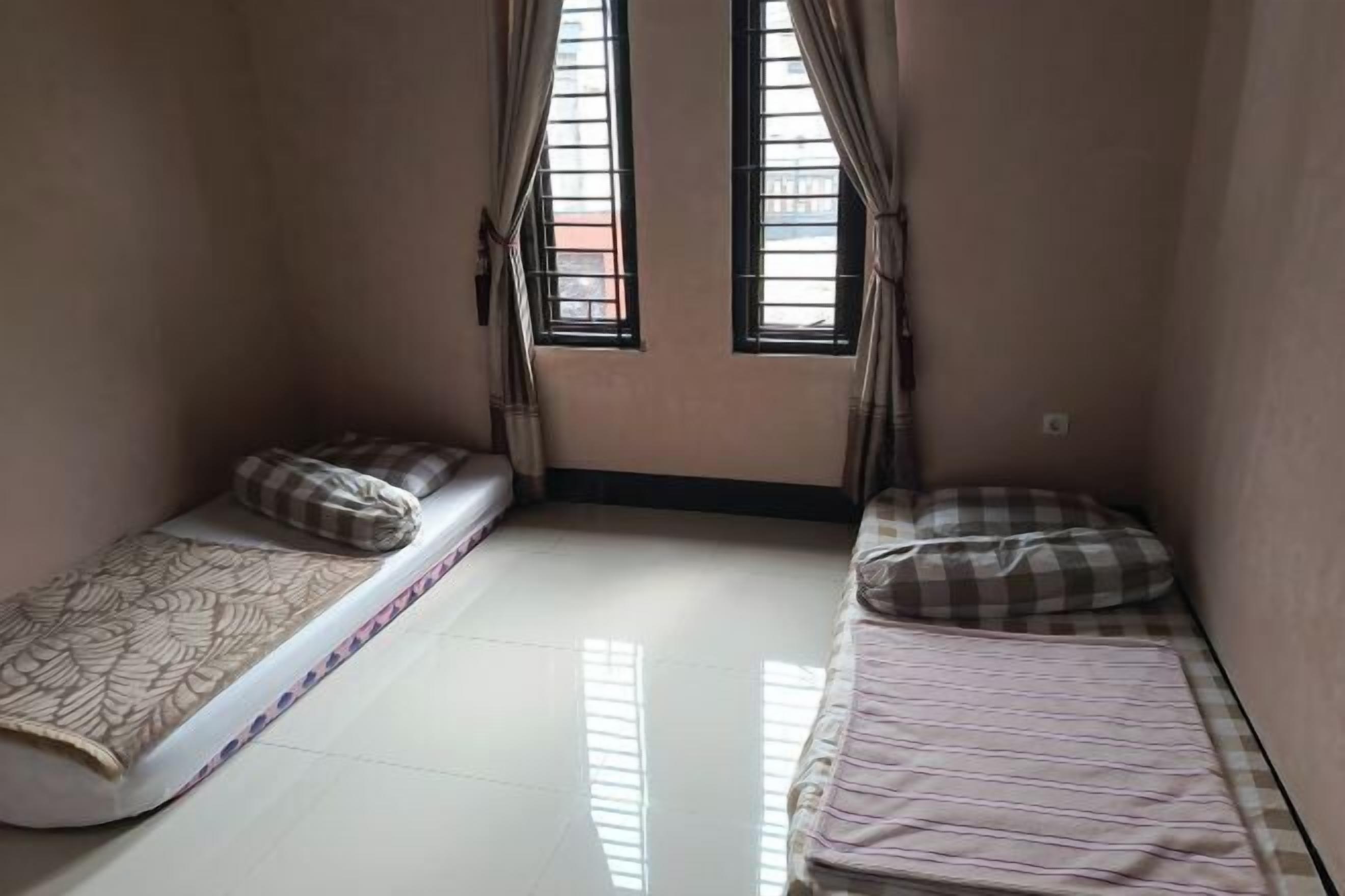 A small room with two single beds, a window with curtains, and a tiled floor.
