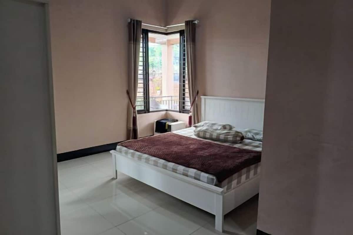 Une chambre à coucher avec un lit, une table de chevet, une fenêtre avec des rideaux et un radiateur.