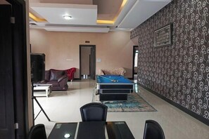 A room with a pool table, a sofa, a dining table with chairs, and a patterned wall. - F_one Village (Cisarua)