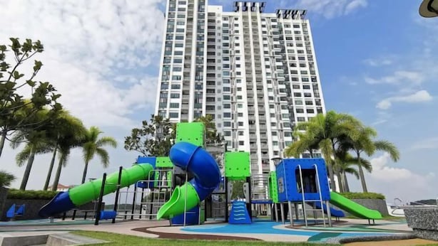 Un parque infantil con toboganes y estructuras para escalar, rodeado de palmeras y un edificio alto al fondo.