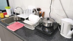 Una cocina con un lavabo, escurreplatos, hervidor y diferentes utensilios.