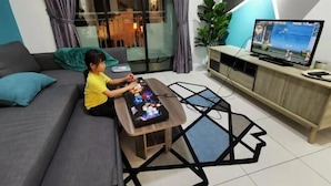 Niño jugando un videojuego en una consola, en una sala de estar moderna con televisor, sofá y puerta de cristal que da a un balcón.