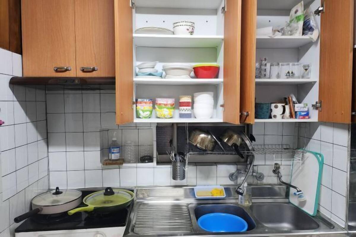 A kitchen with a stove, sink, and open cabinets containing dishes and kitchenware.
