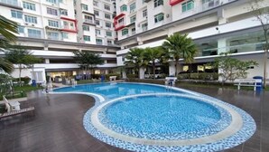 Une piscine dont le bord est revêtu de carreaux, entourée d’une cour plantée de palmiers et bordée d’un immeuble à plusieurs étages doté de balcons.