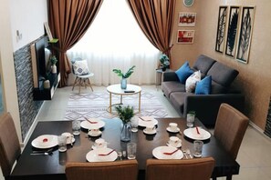 Uma sala de jantar com mesa posta para quatro pessoas, um sofá e uma pequena mesa lateral com uma planta.