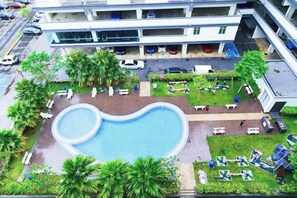 Une piscine entourée de palmiers et de chaises longues, avec un bâtiment en arrière-plan.