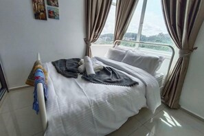 Quarto de hotel com cama, cortinas, janela com vista e uma pequena mesa com toalha.