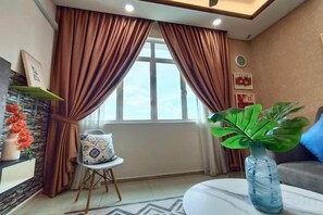 Uma sala de estar com sofá, mesa de centro, poltrona, vaso com planta e janela com cortinas.