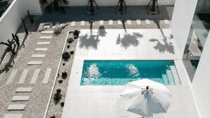 Ein Poolbereich auf dem Dach mit klarem, blauem Pool, umgeben von Liegestühlen, Sonnenschirmen und Palmen.