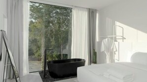 Ein modernes Schlafzimmer mit einem großen Bett, einer schwarzen Badewanne und Blick ins Grüne durch das Fenster.