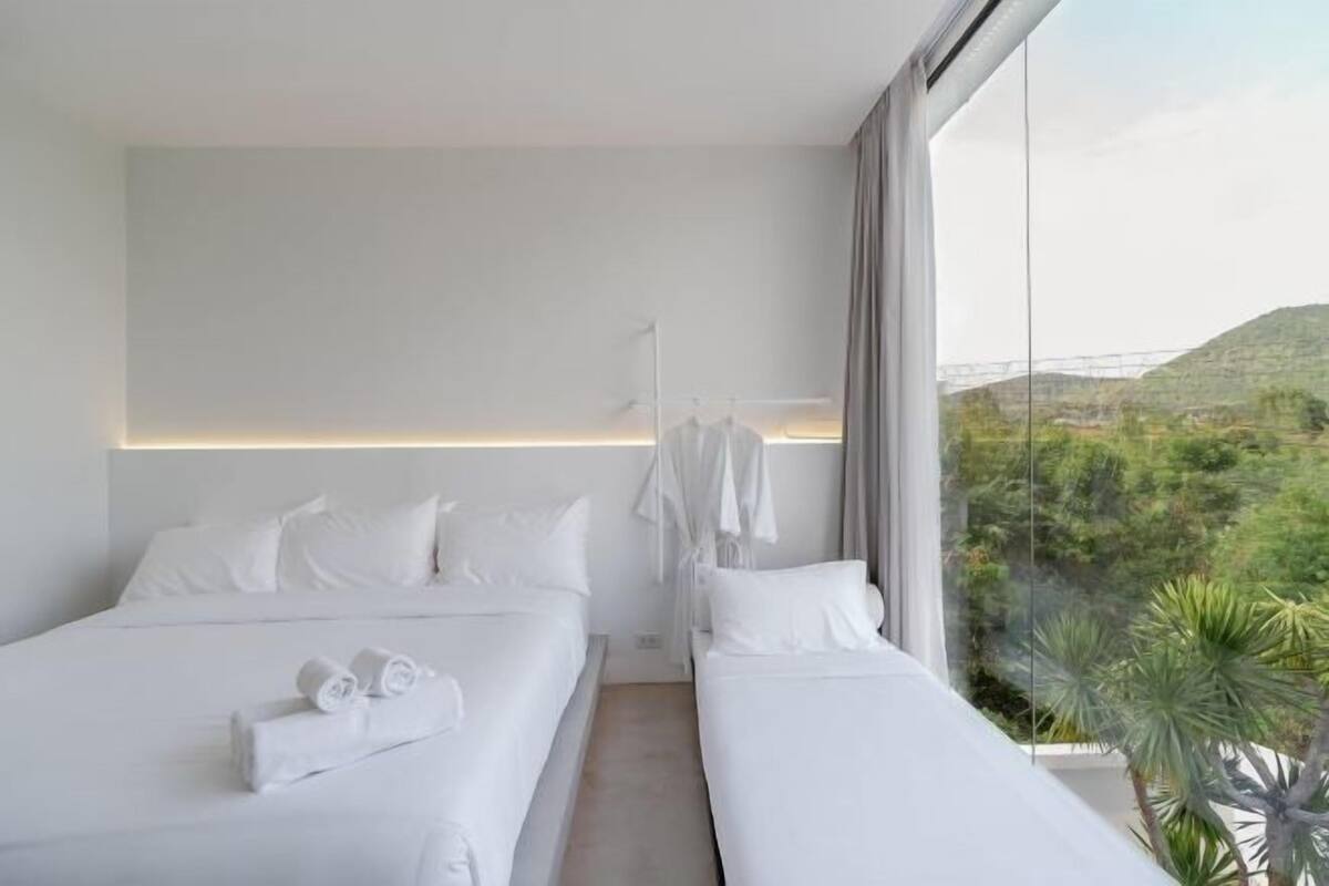 Ein modernes Hotelzimmer mit zwei Betten, einem großen Fenster und Blick auf Grünflächen sowie einem Kleiderständer.