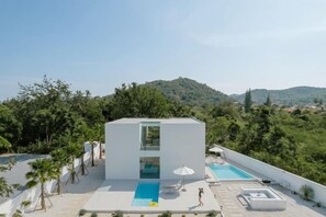 Un edificio moderno con piscina, rodeado de vegetación y colinas.